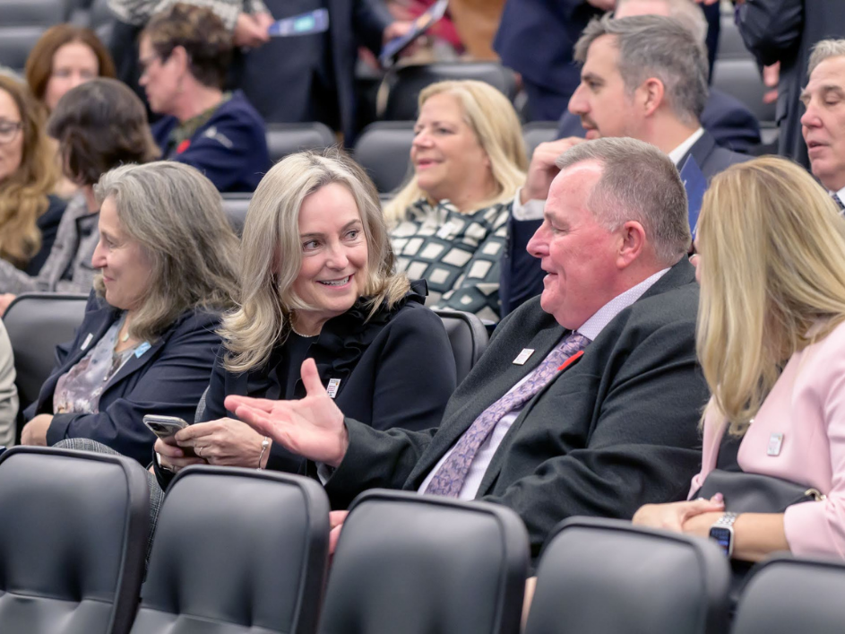 A group businesspeople (two women and one man) conserving while seated in a lecture hall.