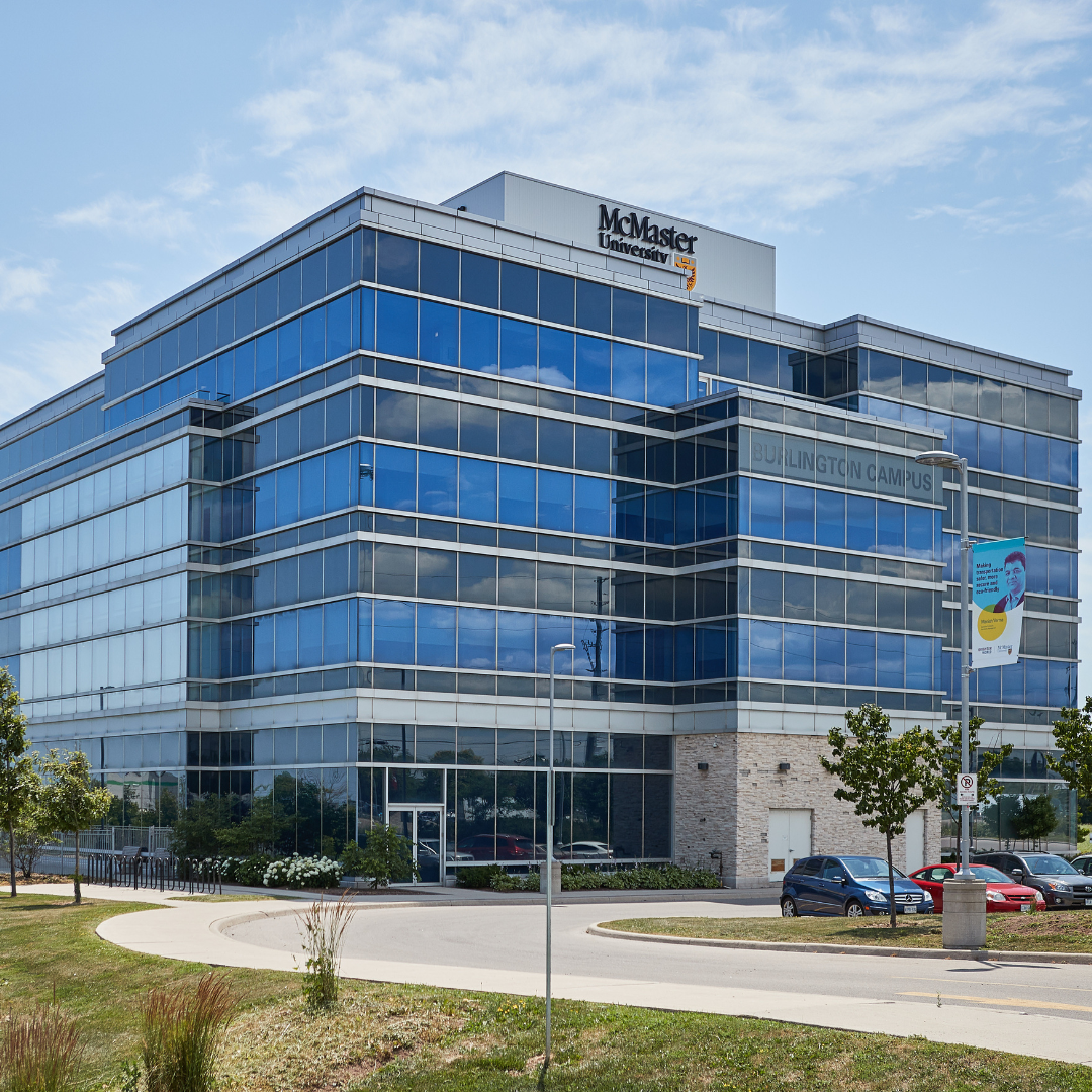Tall modern glass building with a McMaster logo at the top during daytime.