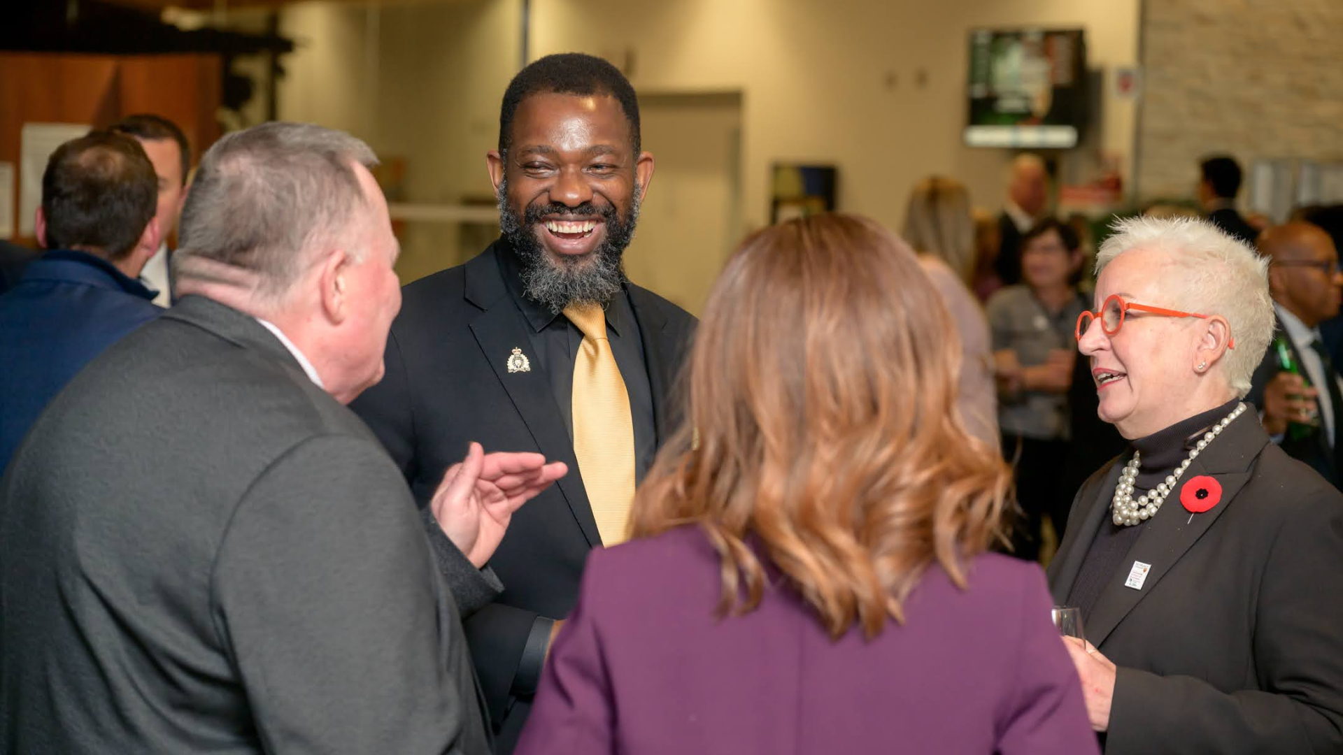 A group of diverse individuals, including a laughing Black man in a suit and tie, are engaged in conversation.