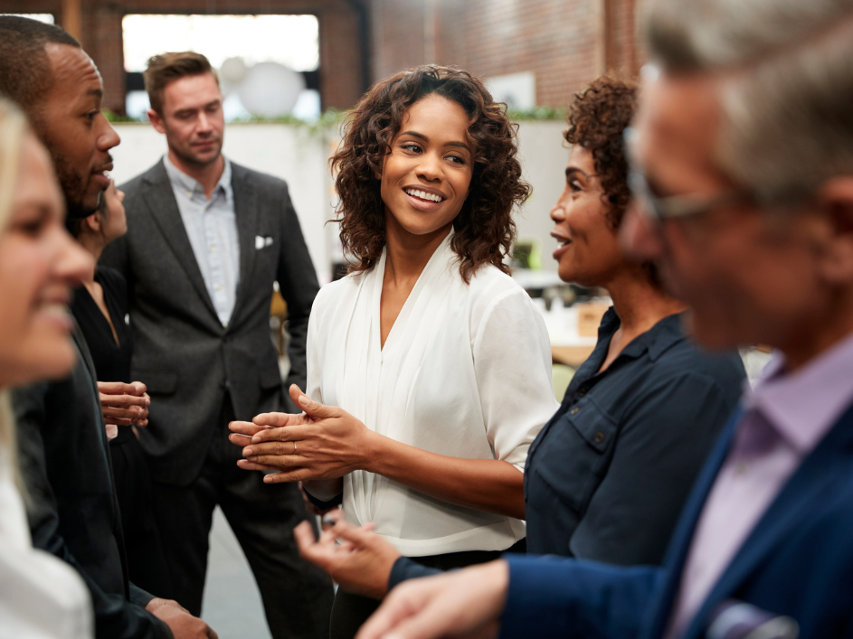 A group of diverse professionals conversing in an office setting.