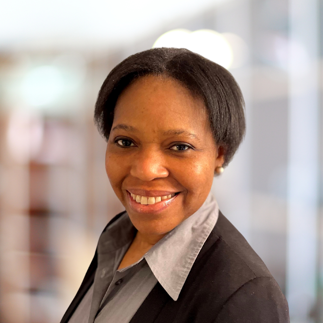 Portrait of Adesua Ezeokafor, a smiling woman with short, dark hair, wearing a black suit.