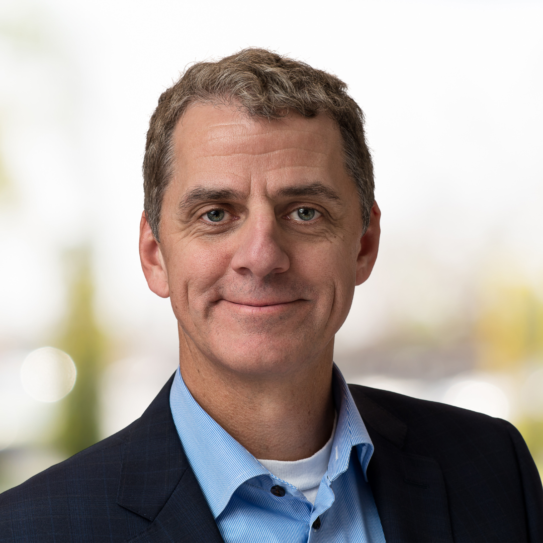 Portrait of Robert Foy, a smiling man with short, dirty blonde hair. wearing a black suit.