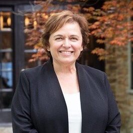 Headshot of Vita Drieberg, smiling in a black suit